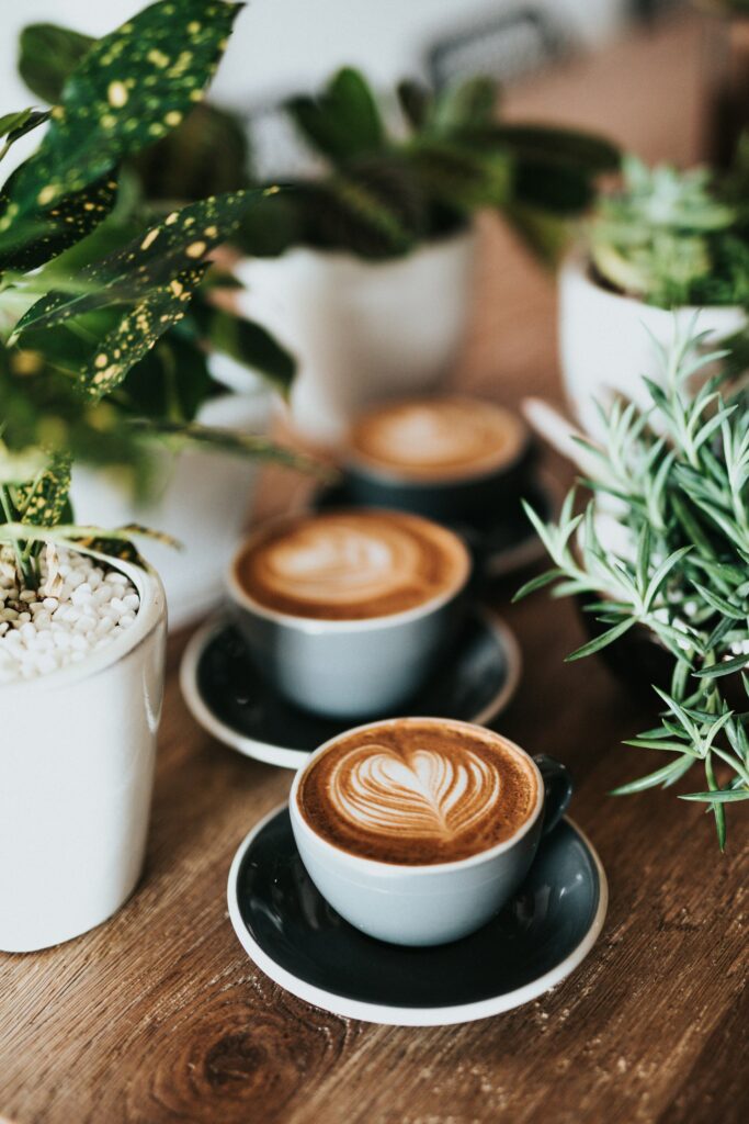 Koffie sfeerfoto met latte art op een houten tafel, omringd door groene planten
