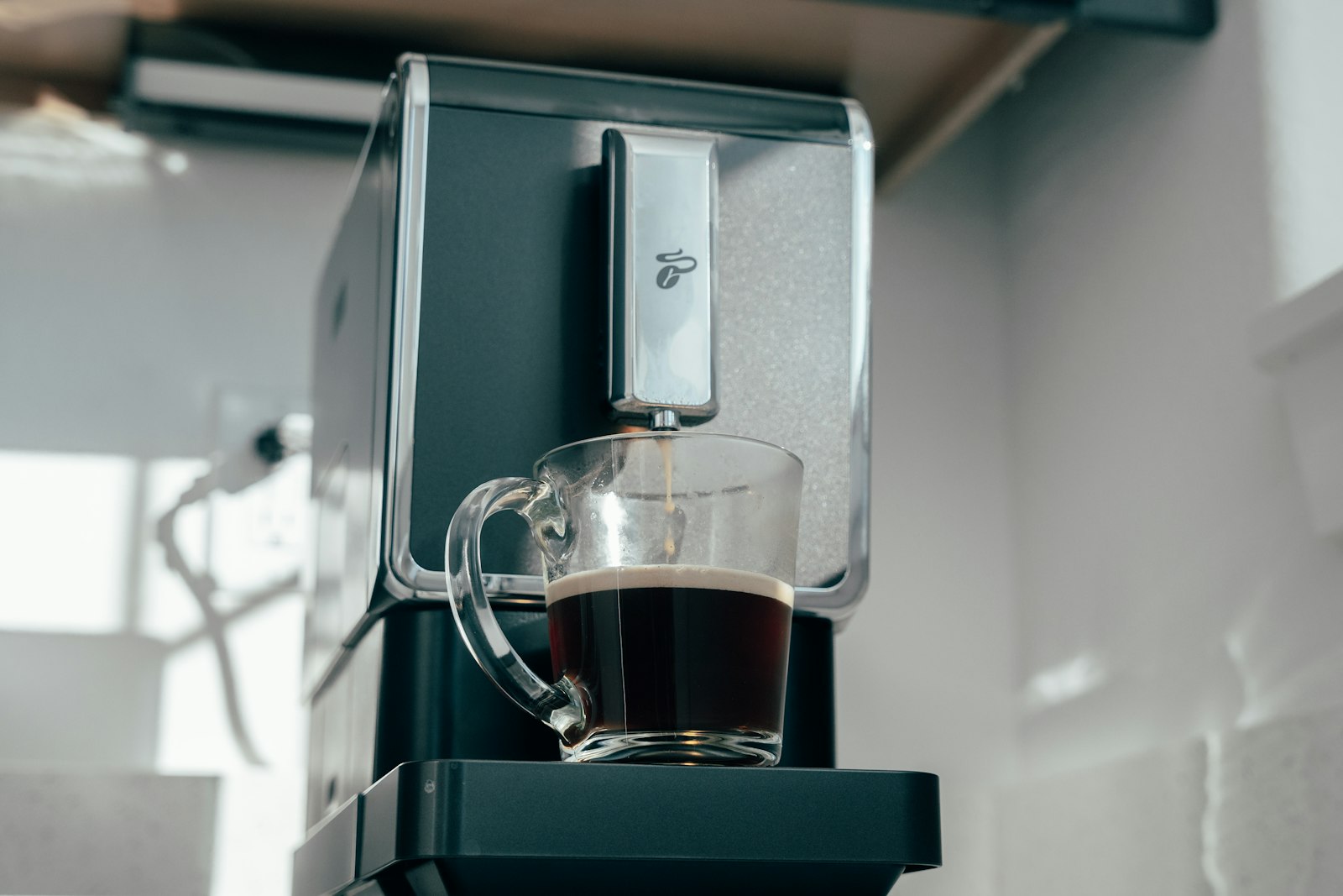 Glazen kop zwarte koffie onder de uitloop van een volautomaat